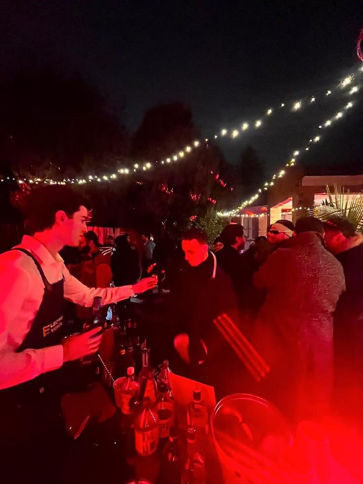 Electric Events bartender serving guests at an outdoor party under festoon lights